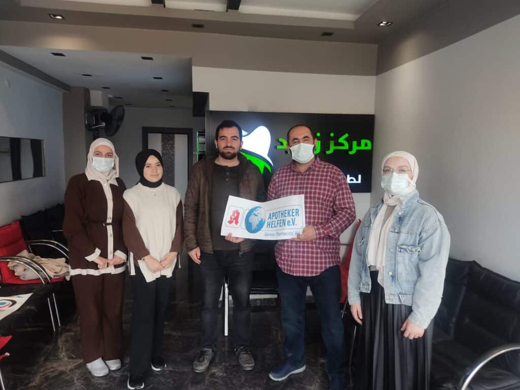 Daylight for All - Unterstützer-Team der Organisation "Daylight for All" posiert in der Praxis. Die fünf Personen halten das Schild des unterstützenden Vereins APOTHEKER HELFEN e.V. (German Pharmacists Aid) in die Kamera, um die Zusammenarbeit zu demonstrieren.